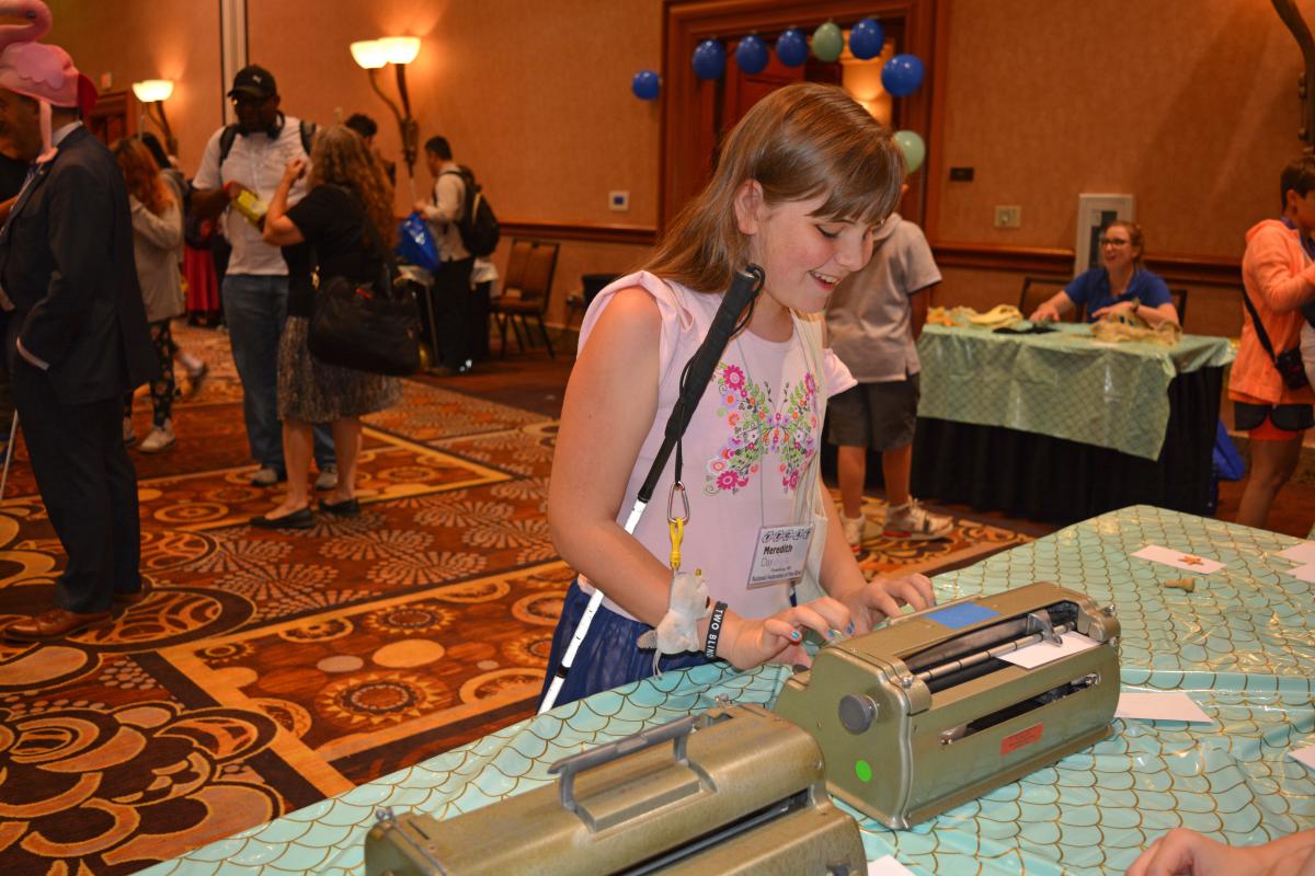 A young girl uses a Perkins Brailler at the Action Fund carnival celebration at the NFB National Convention.