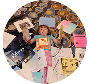 A blind girl smiles while surrounded by a pile of Braille books