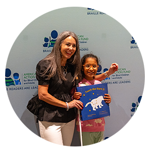 A mother and her blind daughter smile for a photo while holding a print/Braille book