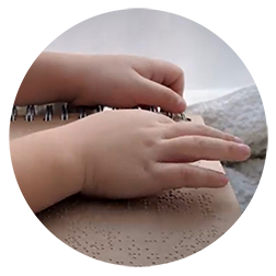 Close up of a young child's hand reading from a Braille book.