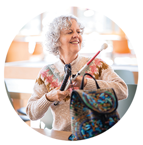 A senior woman smiles in a cafe wile breaking down her long white cane.