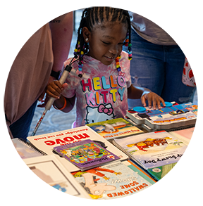 A young girl smiles while checking out a pile of colorful print/Braille books.